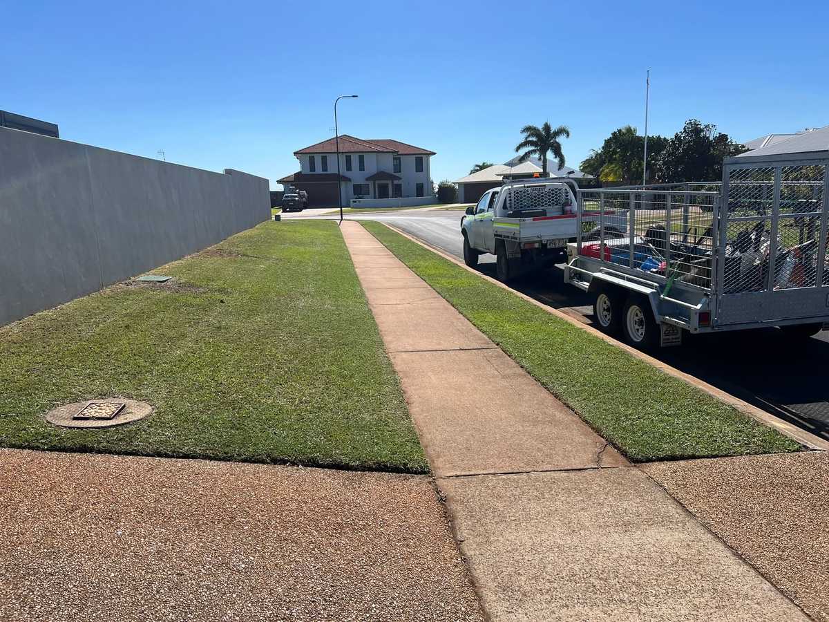 A ute and caged trailer parked at the kerb beside a freshly mown verge
