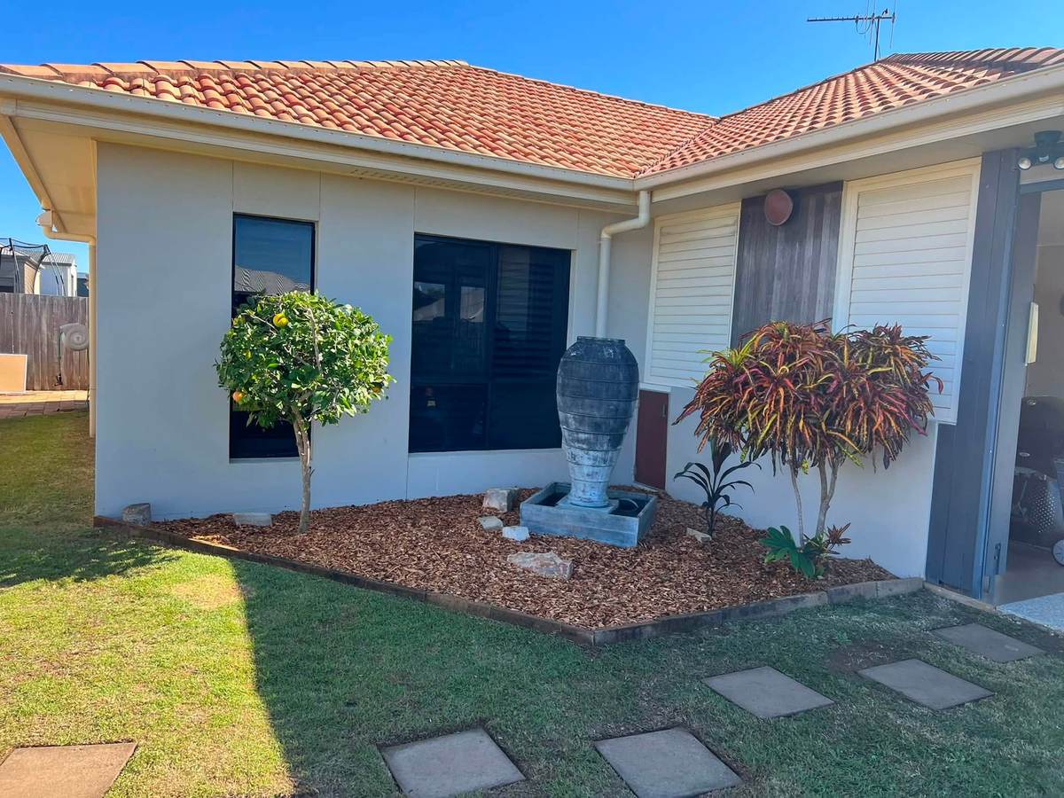 A front yard with pavers, a small tree and a planted bed beside the house