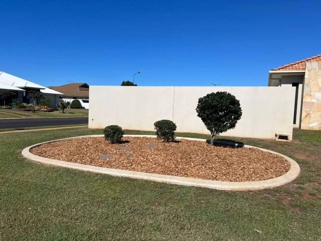 A round garden bed of shaped shrubs and mulch beside a rendered wall