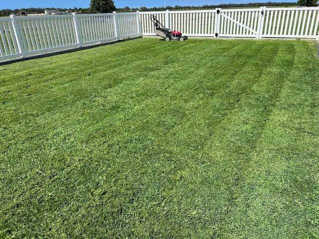 A mown lawn with a white fence and a mower parked at the far side