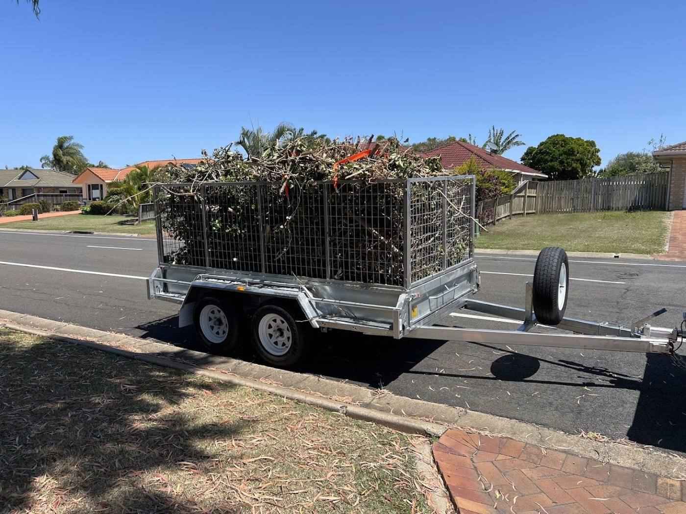A tandem trailer loaded high with cut branches and garden waste